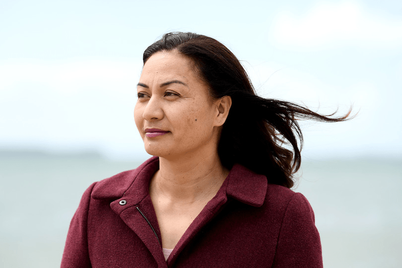 a brown skinned woman in a maroon shirt with a lapel collar and the grey green ocean in the background