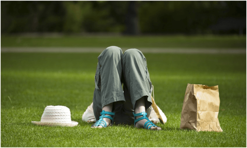 Person lying on their back on grass, we see their bent knees, a hat and paper bag beside them.