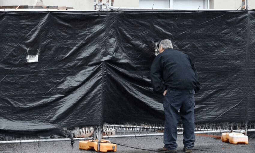A man peers through security fencing at an isolation facility in Rotorua. (Photo by Fiona Goodall/Getty Images) 
