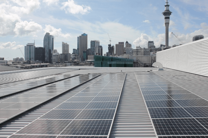 solar panels on the roof of a building with Auckland's skyline of high rises, including the Sky Tower in the background