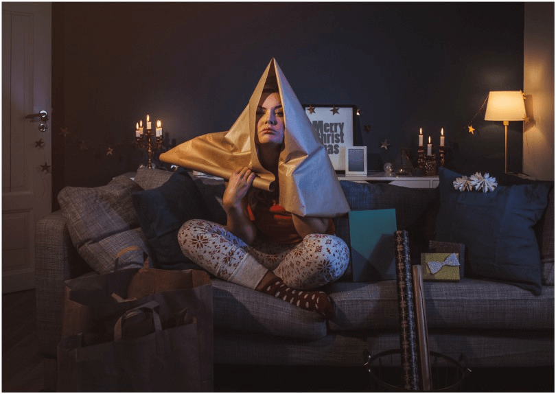 Woman on couch with wrapping paper over head, looking stressed