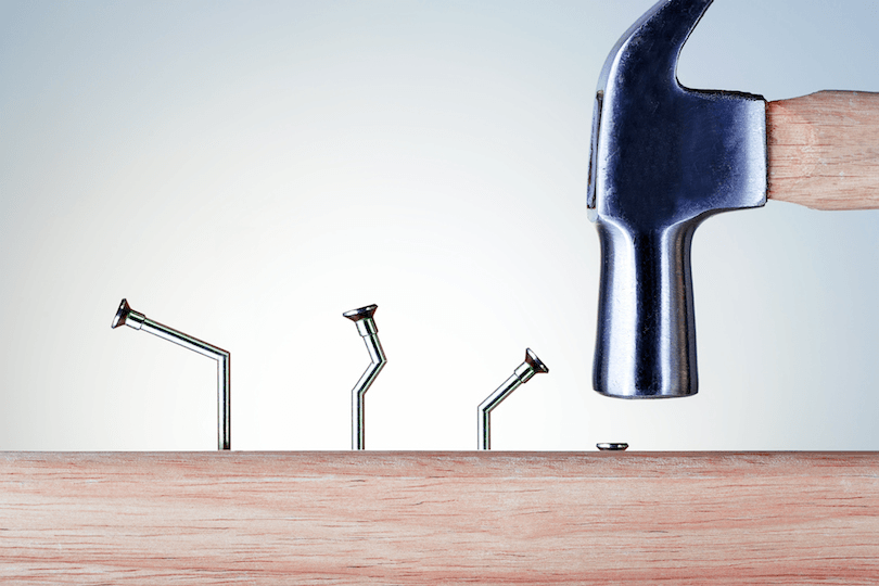 Three bent nails and a hammer driving a fourth in straight