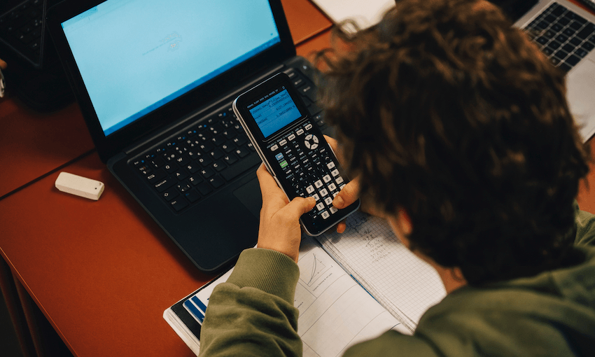 High angle view of teenage boy using calculator while studying over laptop at desk in classroom
