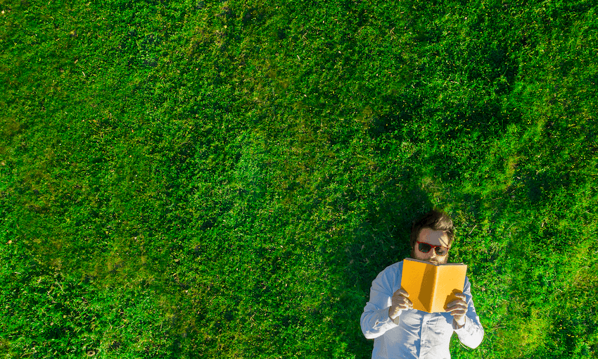 Aerial photo of young man lying in bright green grass, reading