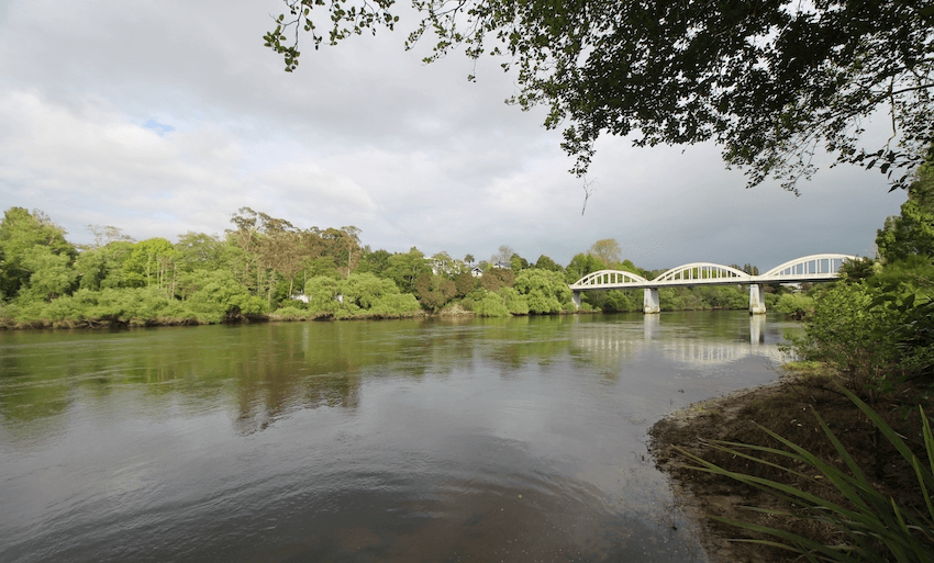 a brownish green river running under a white bridge and a sky heavy with water