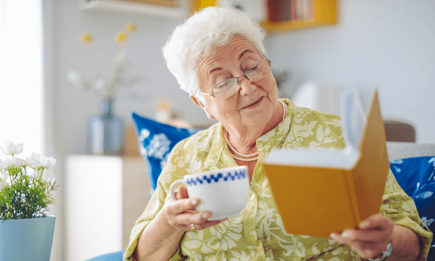 Senior woman holding a cup of tea and a book, looking delighted