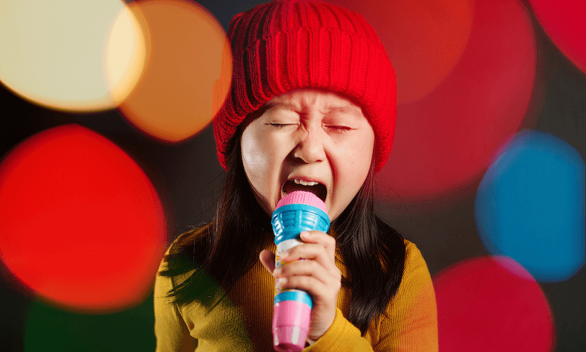 Young girl wearing red beanie, singing into karaoke mic, colourful lens flare in background