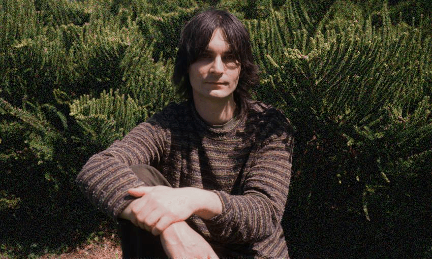 kane strang sitting in front of green bushes, hands clasped casually