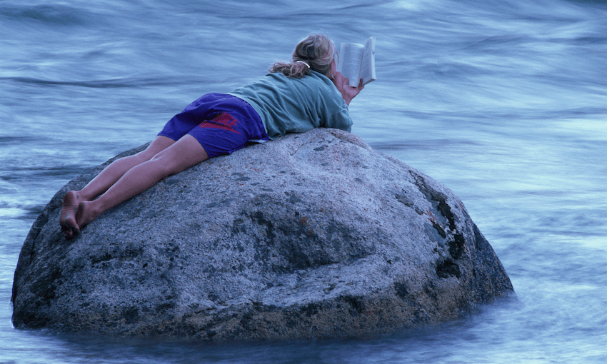 A woman lies on a rock in the middle of a river, reading