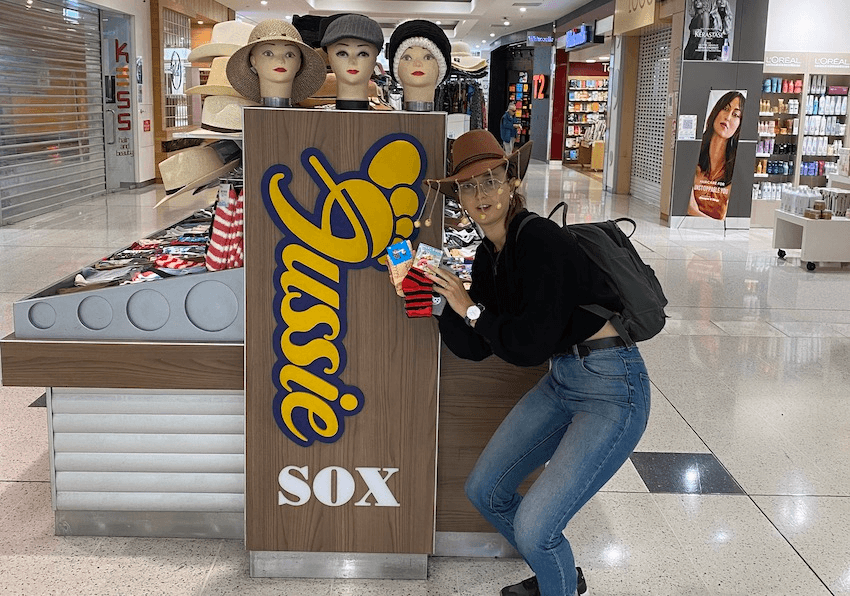 Author squats next to Aussie Sox stall at mall, holding up three pairs of socks.