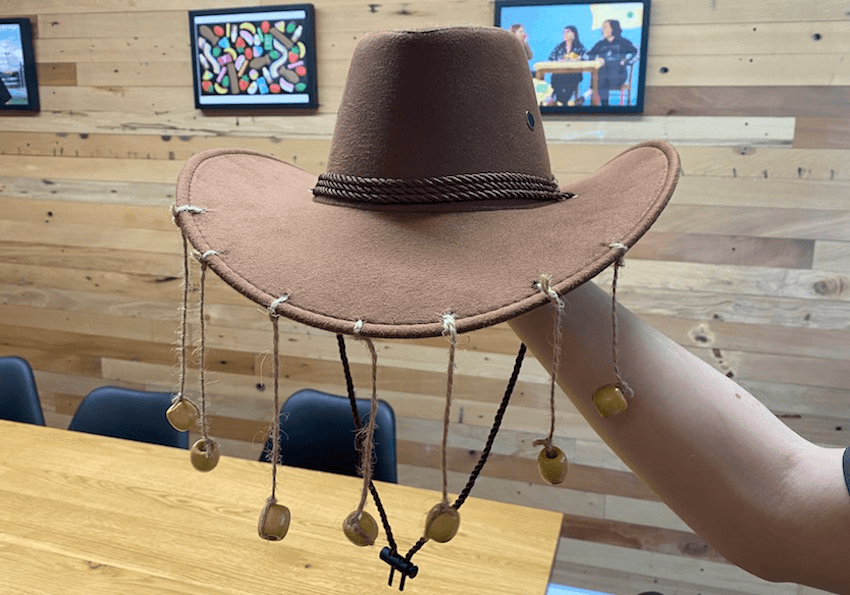 An arm holding up a hat with jute twine and beads strung off its front.