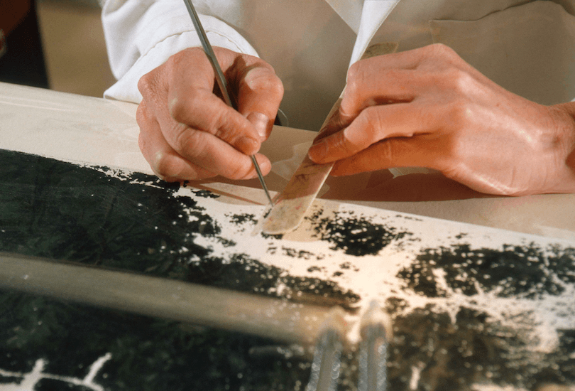 Hands of a conservator carefully working on an area of damaged paint