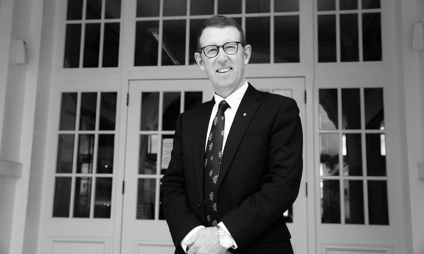 Patrick Drumm with his hands clasped in front of him, stands in front of the MAGS main entrance, smiling.