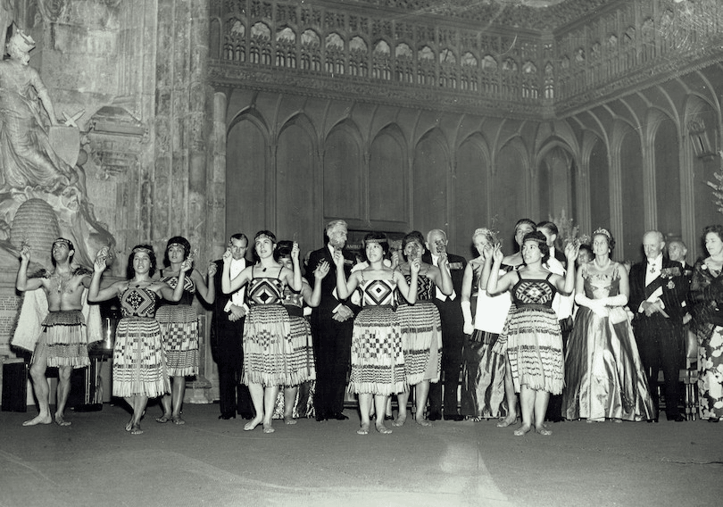 A black and white image of a pōwhiri, men and women in evening dress in background.