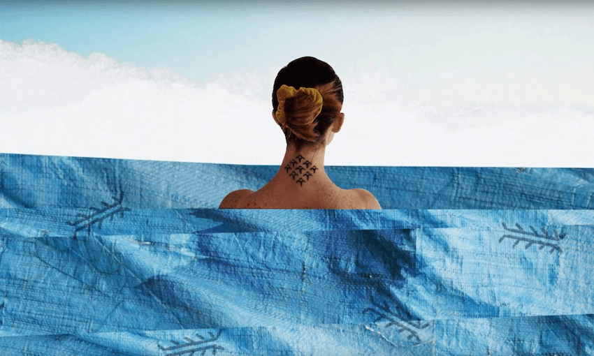 We're looking at a woman standing in the sea, her back to us, hair up showing the tattoo on her neck. The sea is a collage.