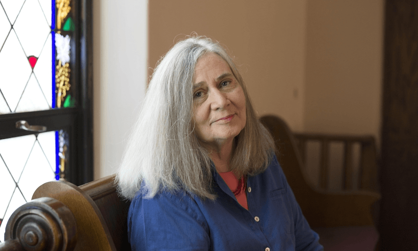 An older woman sits in a church pew, serene, smiling, stained glass window behind her.