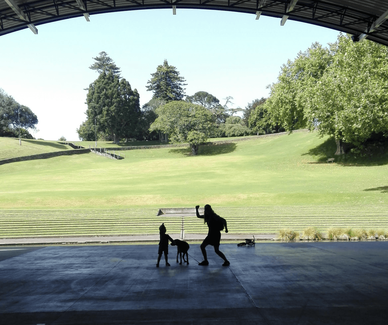 Yahoo! We're inside a soundshell in a park, looking out at a woman, a child and a dog silhouetted against the light. The woman and child are punching the air in celebration. 