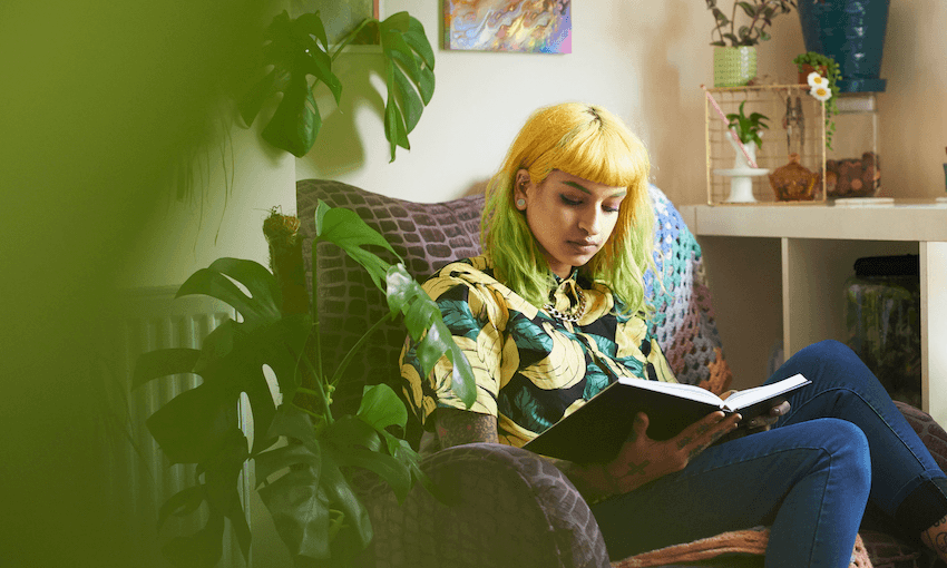 A living room filled with houseplants; a young woman reads on an armchair.
