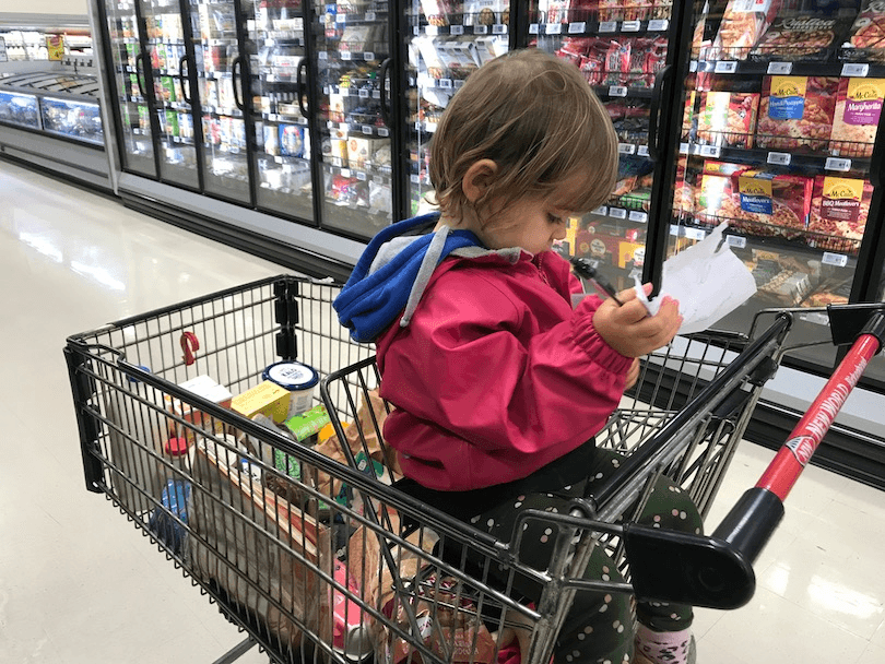 Toddler in trolley at supermarket, trolley loaded with pudding ingredients