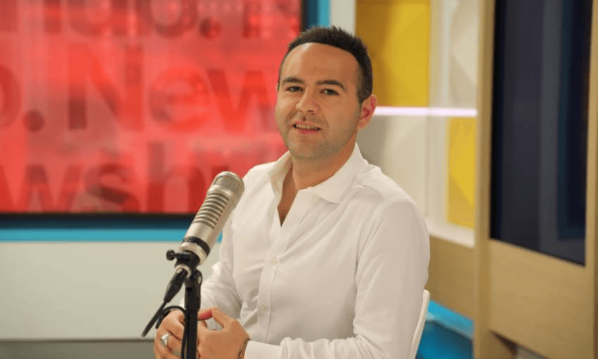 Aziz Al Sa’afin sits at his TV desk in front of a microphone, smiling
