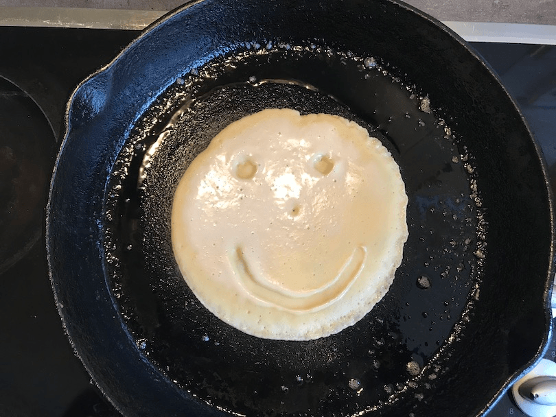 Pancake cooking in cast-iron pan, smily face in batter