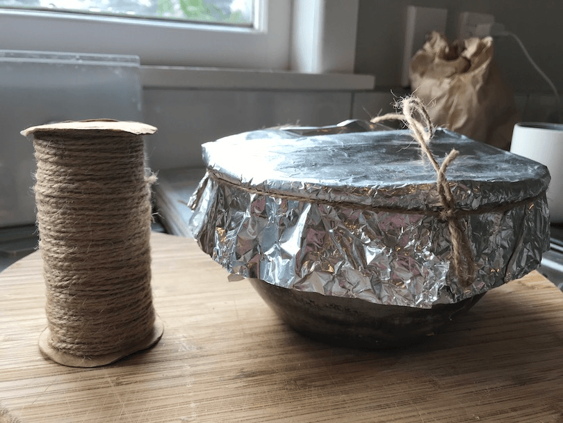 A reel of string and a bowl covered in tinfoil, on a chopping board