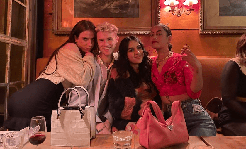 Four friends posing on a couch at a bar. Scene tinged with pink from the lights.