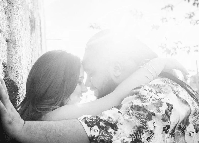 Black and white photograph of couple forehead to forehead, woman leaning back against a tree. Beautiful light.