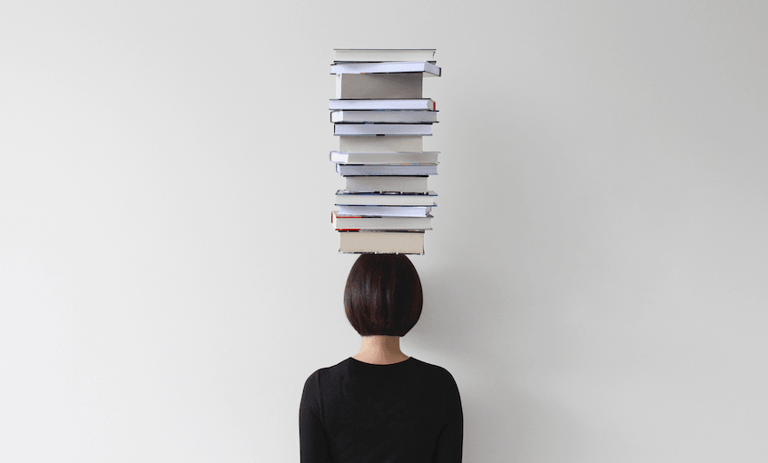 Photograph of woman with books stacked on her head; we're seeing her from behind