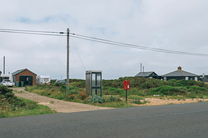 Bleak scene of a road with pebbled driveways, flat horizon, powerlines. Dungeness in the UK.