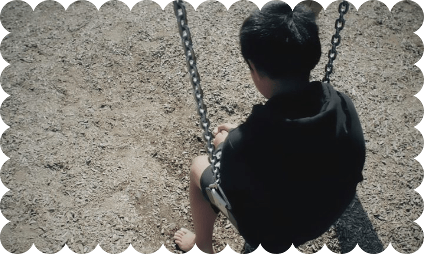 a kid with short hair and a black hoodie sitting on a swing with their back to the camera and it looks sad and lonely