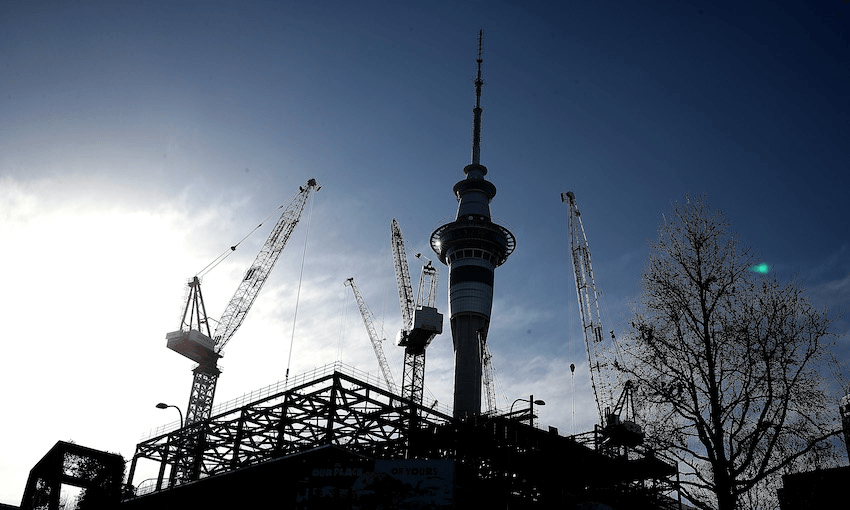 A clear day, the Skytower silhouetted, huge cranes rising up all around it, construction in the foreground