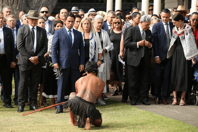 A crowd of people in suits are welcomed onto a marae