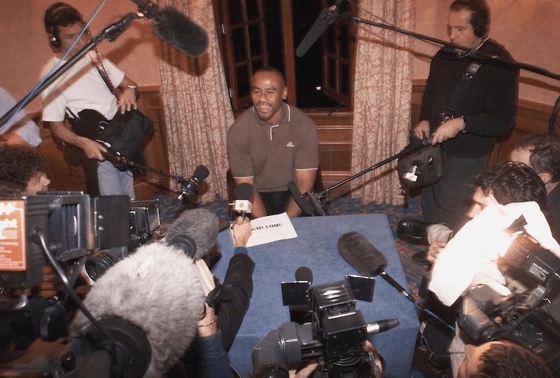 Old photo of Jonah Lomu seated at table surrounded by media, sound booms and mics etc
