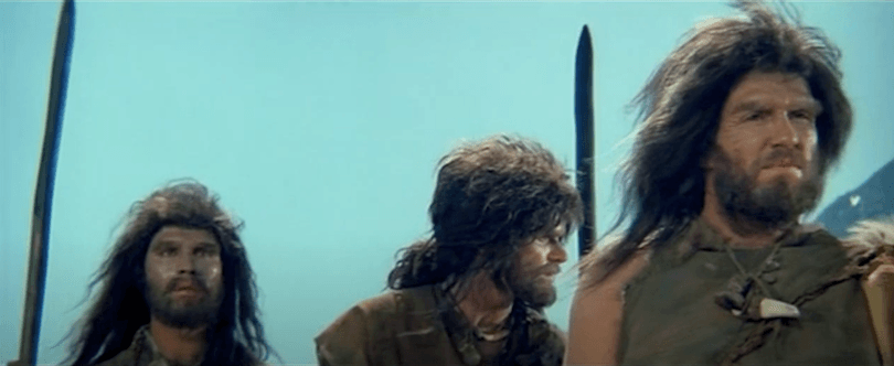 Still from an old film showing three actors dressed as Neanderthals. Terrible wigs. 