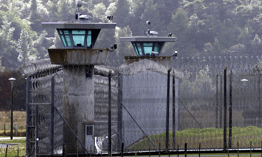 Exterior view of a prison yard and guard towers, backdrop of native bush