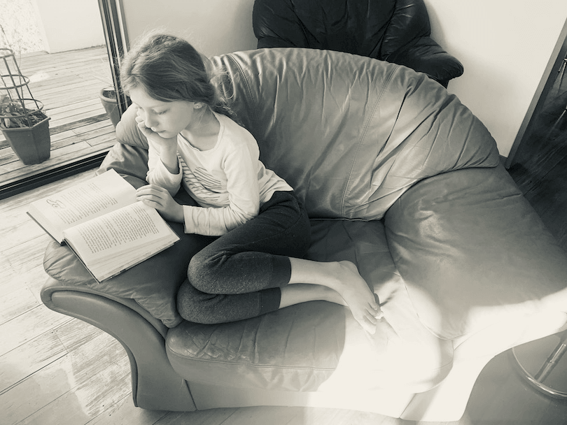Black and white photo of a girl curled up reading in a patch of sunlight on a big cushy chair