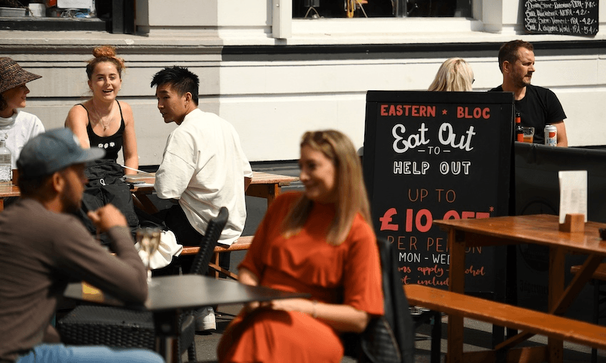 Diners sit near a sign promoting the British government’s ‘Eat out to Help out’ scheme to get consumers spending again after lockdown, in Manchester, August 2020 (Photo: OLI SCARFF/AFP via Getty Images) 
