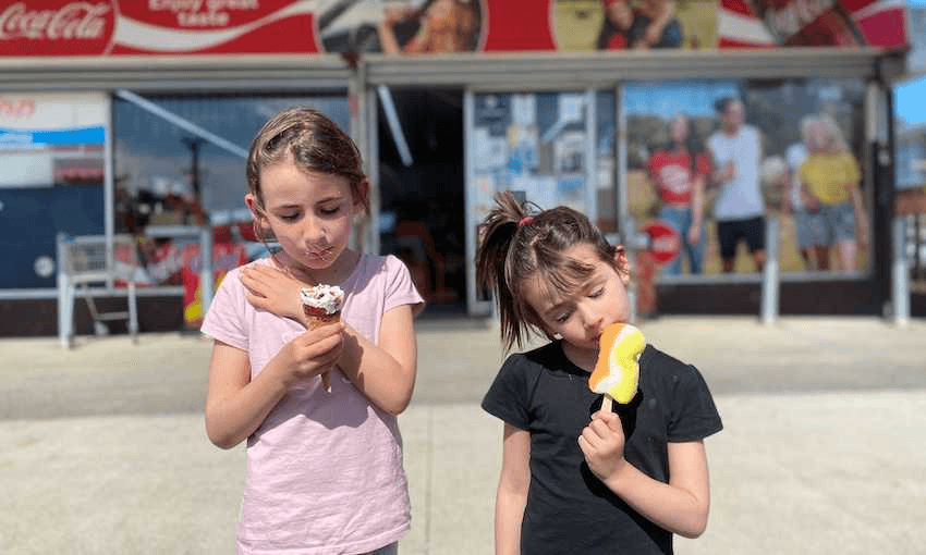Two young girls lick iceblocks outside an Auckland dairy.