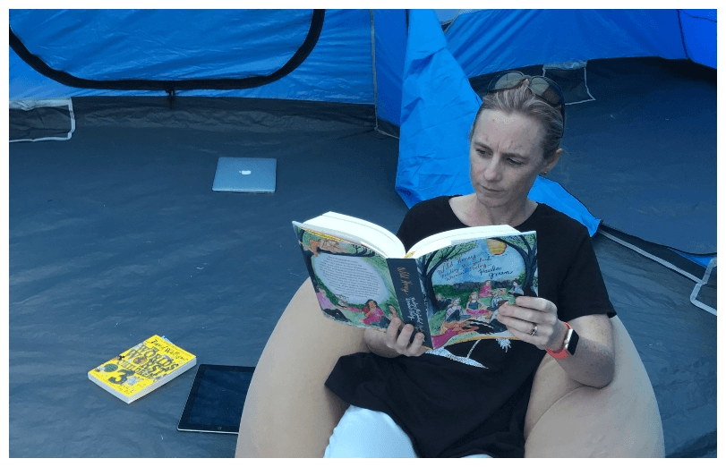A woman on a beanbag, reading a book of poetry, in a tent