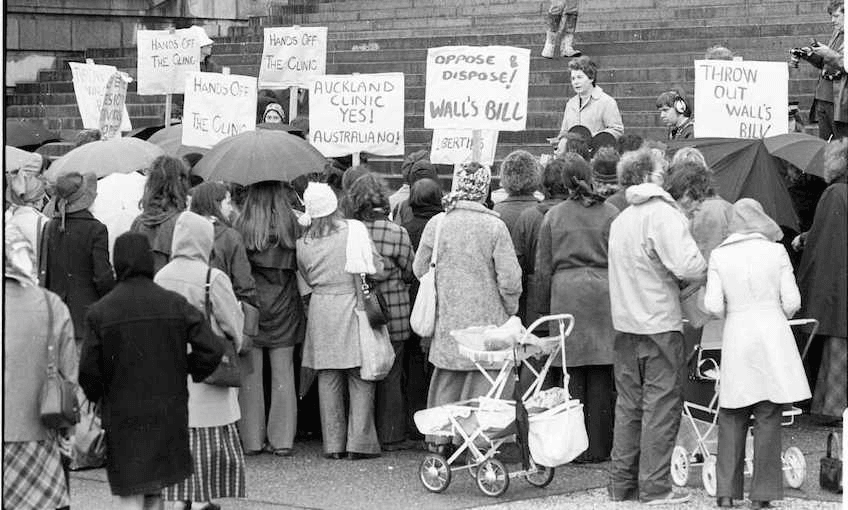 Old black and white photograph of a few dozen protestors, mostly women, with baby carriages parked behind. Holding placards in support of the right to legal abortions.