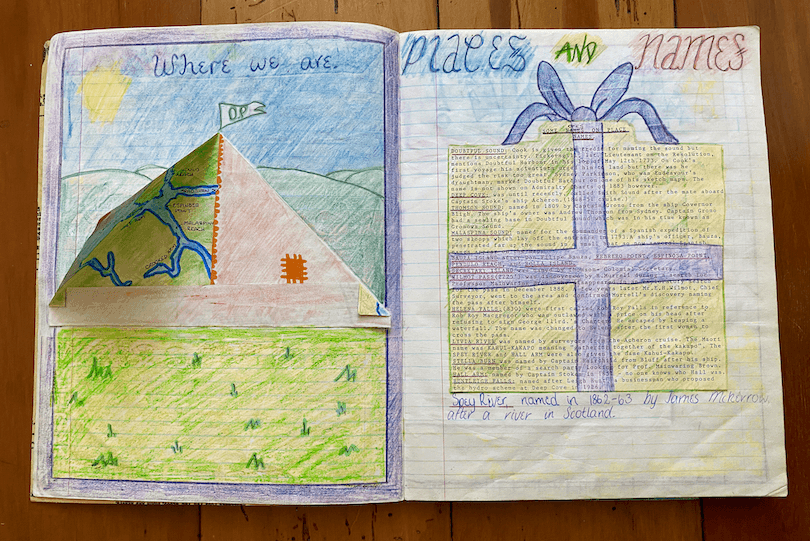 A spread of an old school work book, showing beautifully coloured-in projects on Fiordland, including a pup tent with flaps that open. 