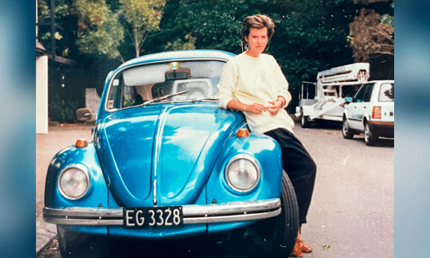 Photograph of a young, beautiful woman leaning comfortably against a old, blue VW Beetle. She looks very happy.