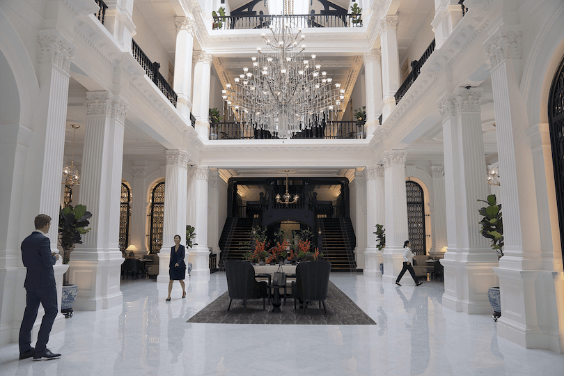 Photo of the interior of the Raffles Hotel Singapore lobby – it's all gleaming white marble and impeccably-dressed staff, also a chandelier