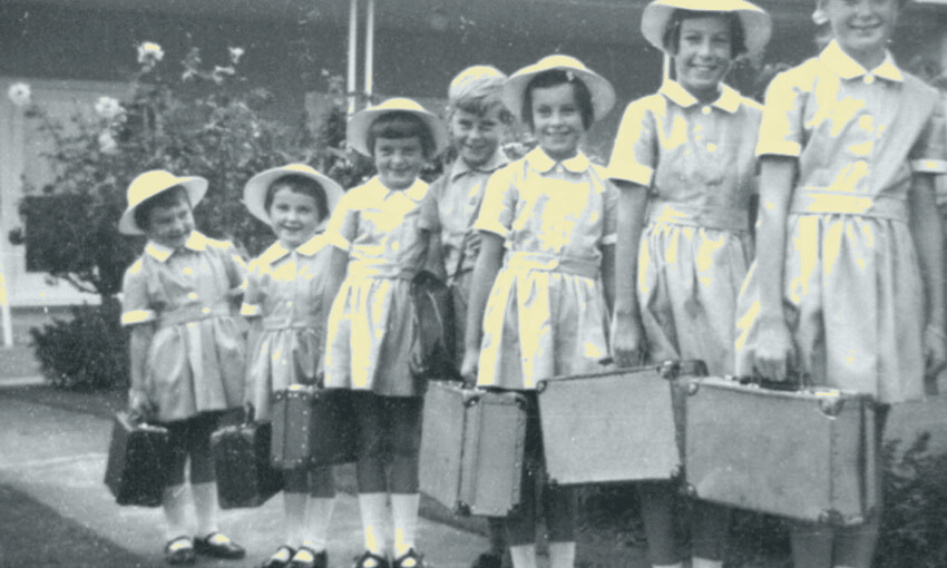 Charming old black and white photo of a line of school children, all in school uniforms holding little suitcases.