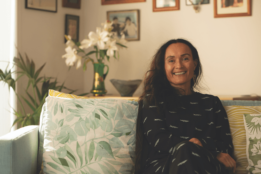 Tahu kukutai sits on a couch and looks at the camera smiling