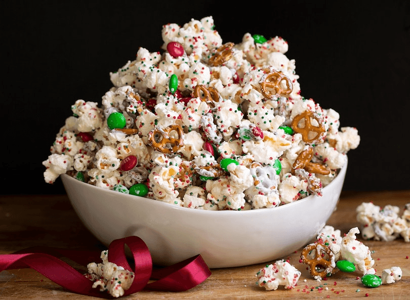 a picture of popcorn drizzled in white chocolate with pretzels adn m&ms.