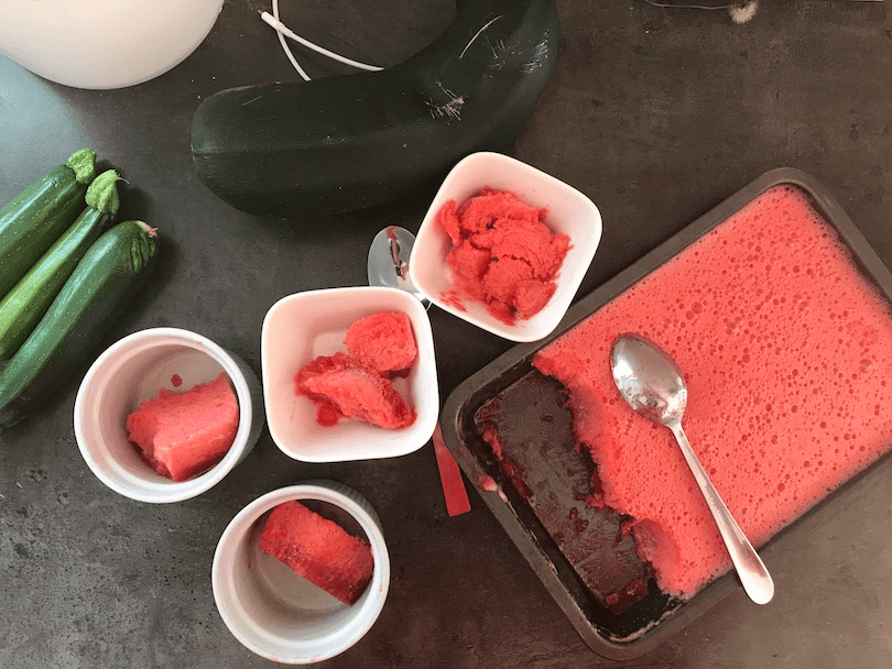 A bunch of ramekins filled with scarlet sorbet, next to a tray of same. Random courgettes all over the place, and a huge marrow. 