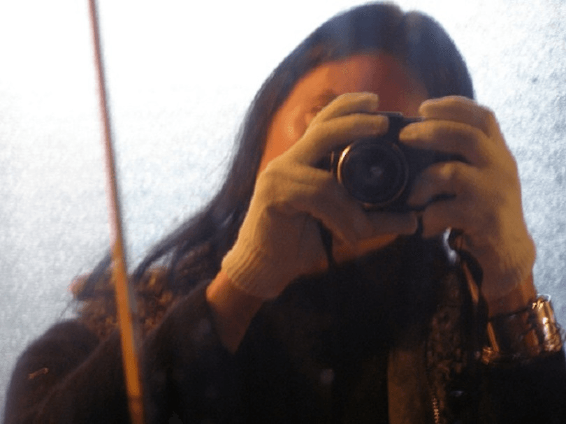 Selfie of woman holding camera in front of face. We can see she has long dark hair. 