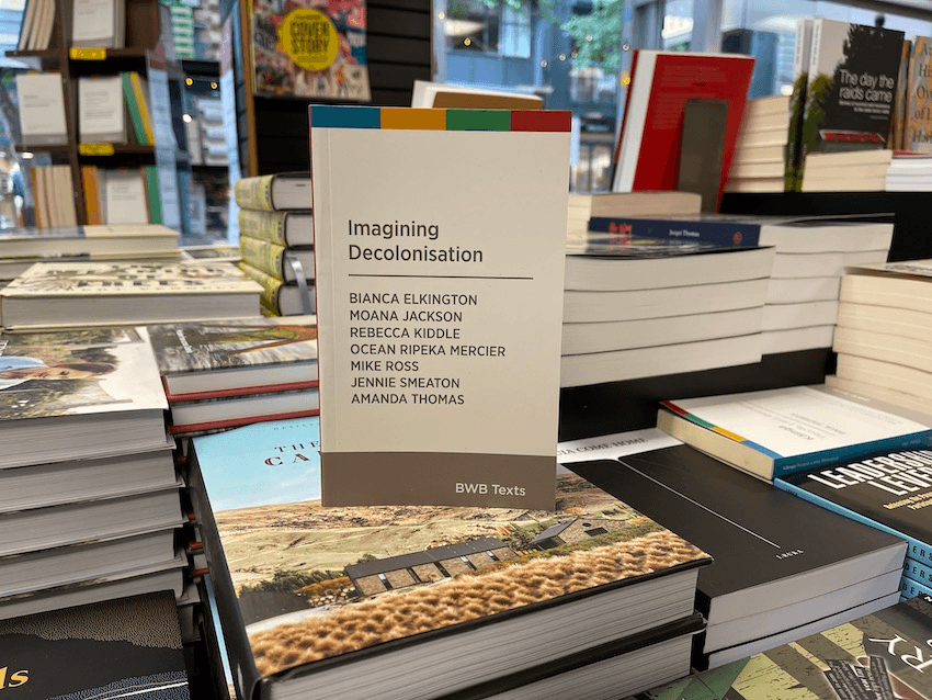 Photo of a book standing upright on a table of books laid flat.